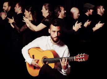 A picture of Daniel Martinex with a guitar and the company behind him.
