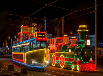 Picture of two illuminated trams, one shaped as a steam engine, the other one as a boat.