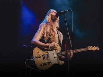 A oicture of Joanne Saw Taylor singing with a guitar.
